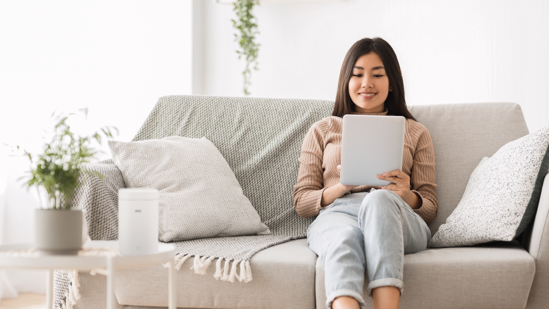 A busy woman sitting on a couch in her minimalist living room, waiting for her meal to cook with a min mini rice cooker.