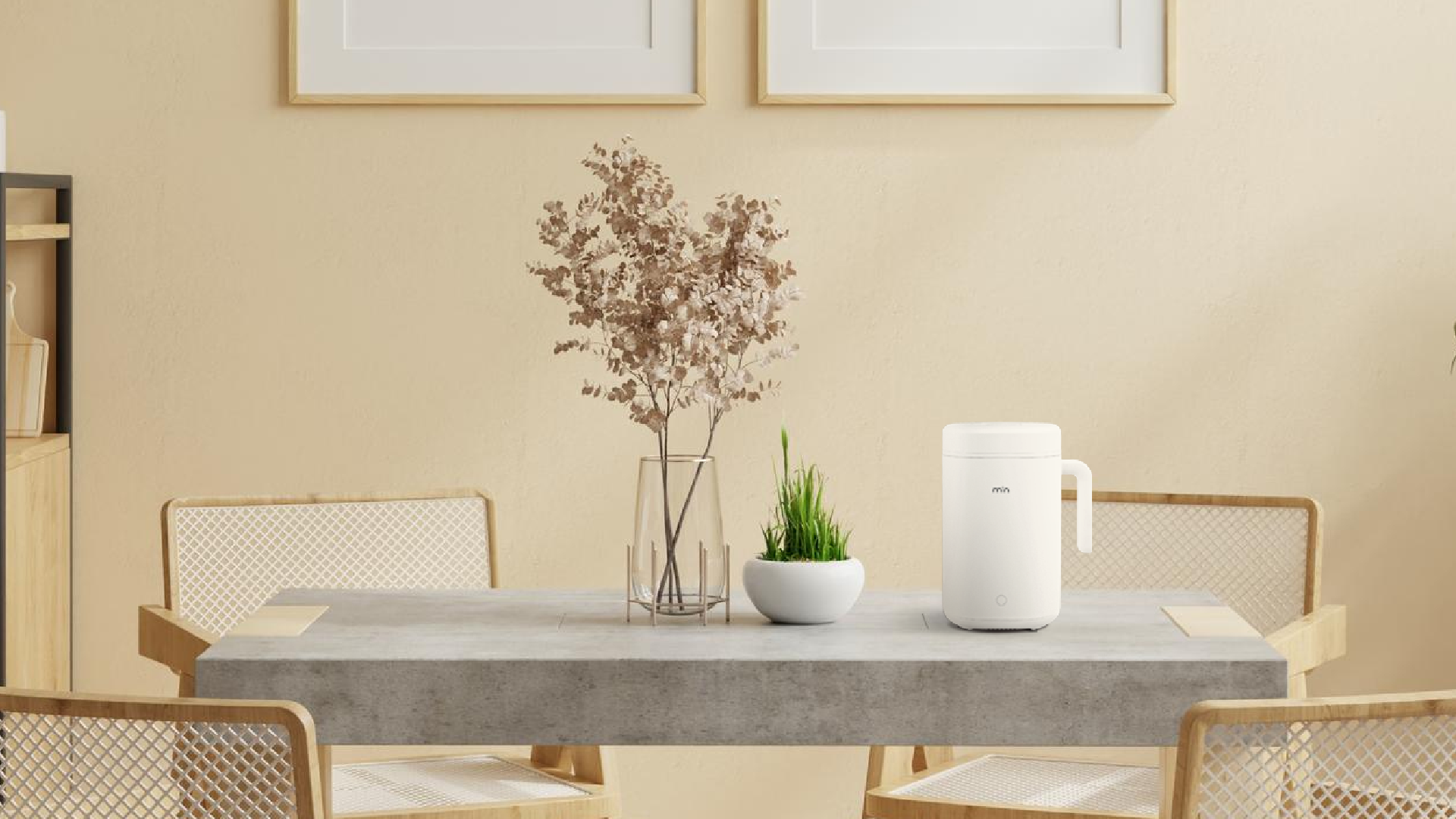 A minimalistic dining room with a gray table, two wooden chairs, a vase with dried flowers, a small potted plant, and a min rice cooker. Two framed pictures hang on the beige wall.